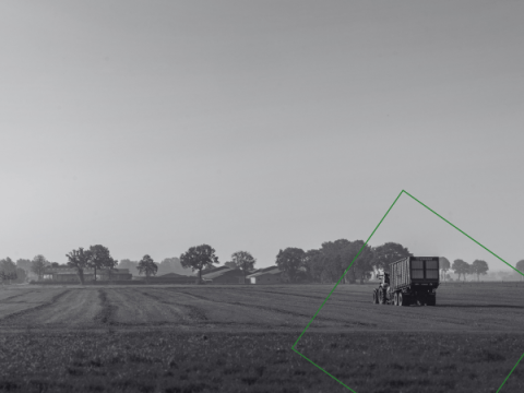 Een tractor met aanhangwagen rijdt op een veld.