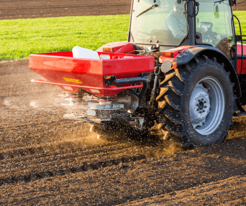 Landbouwer in tractor die kunstofmest strooit